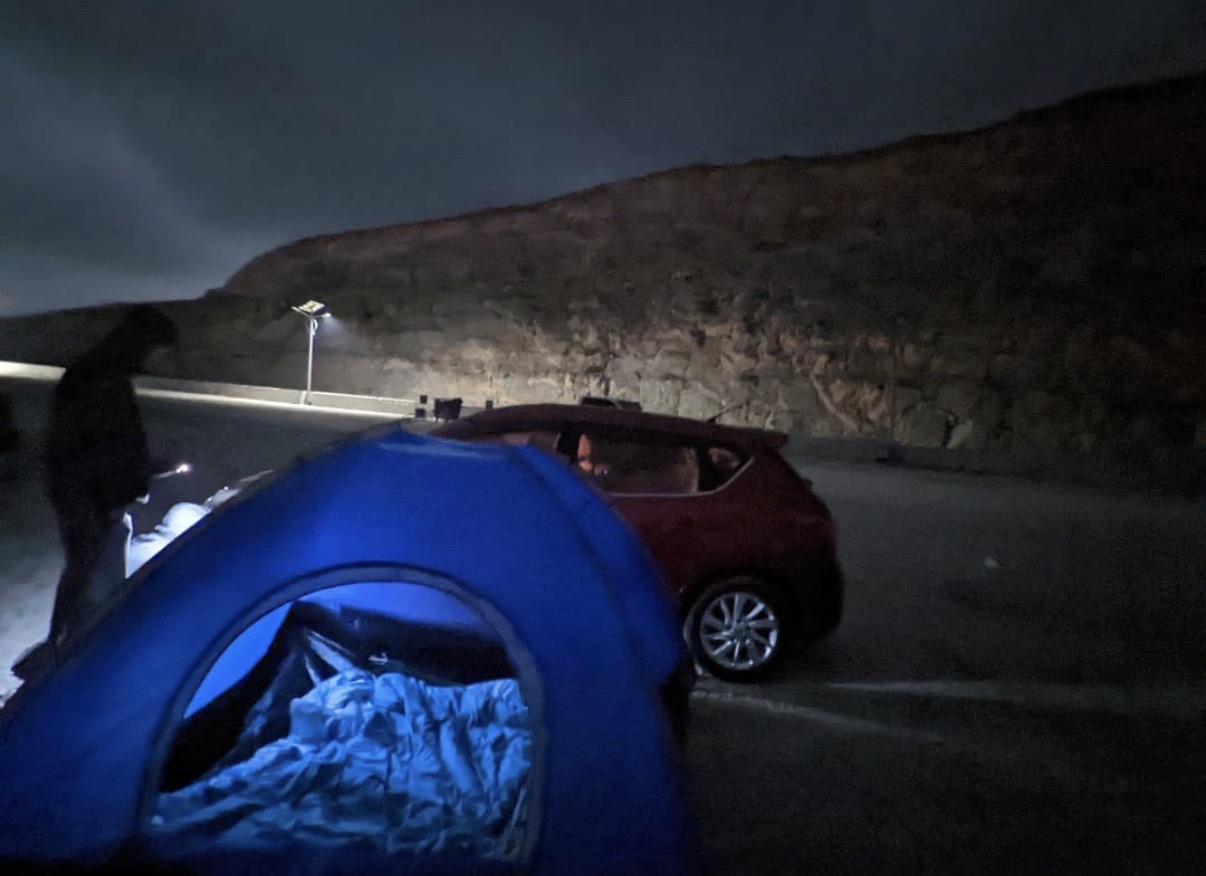 A blue tent pitched beside a mountain road at night