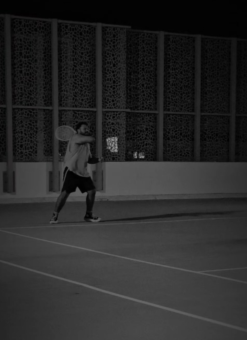 Aman returning a tennis ball on a court at night