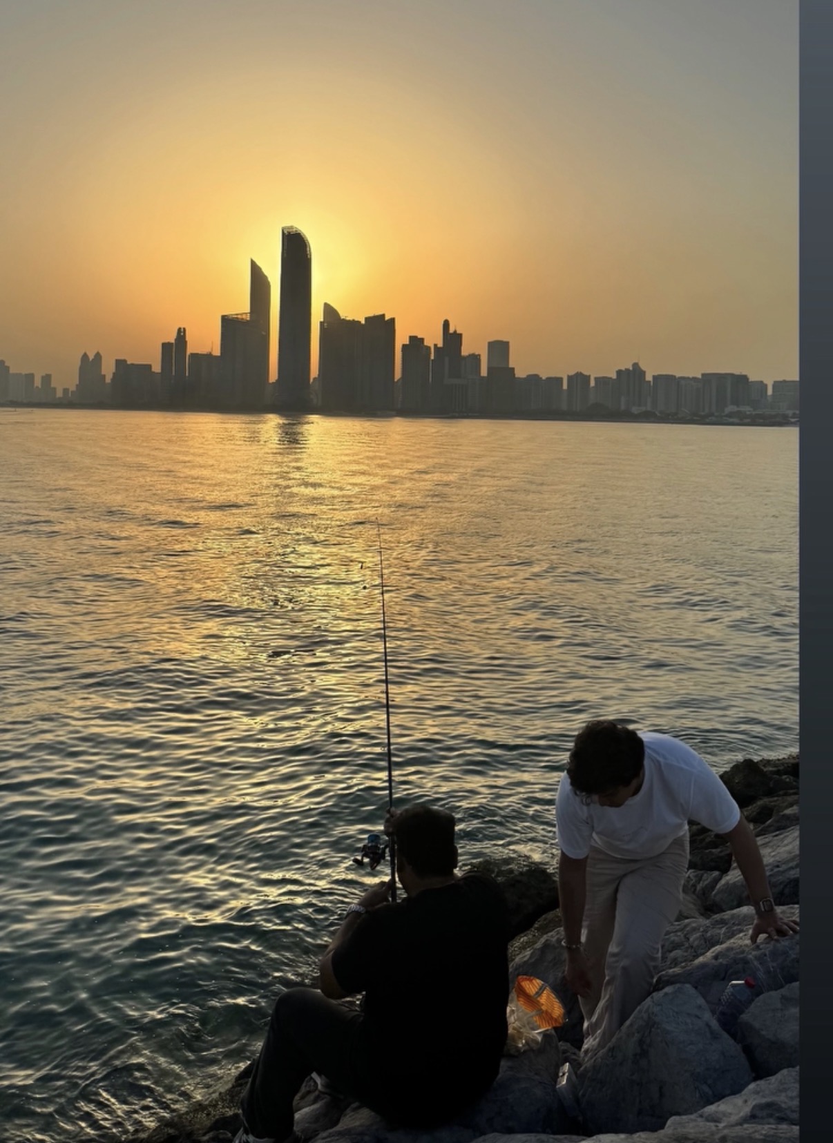 Two friends fishing on rocks against a golden city skyline
