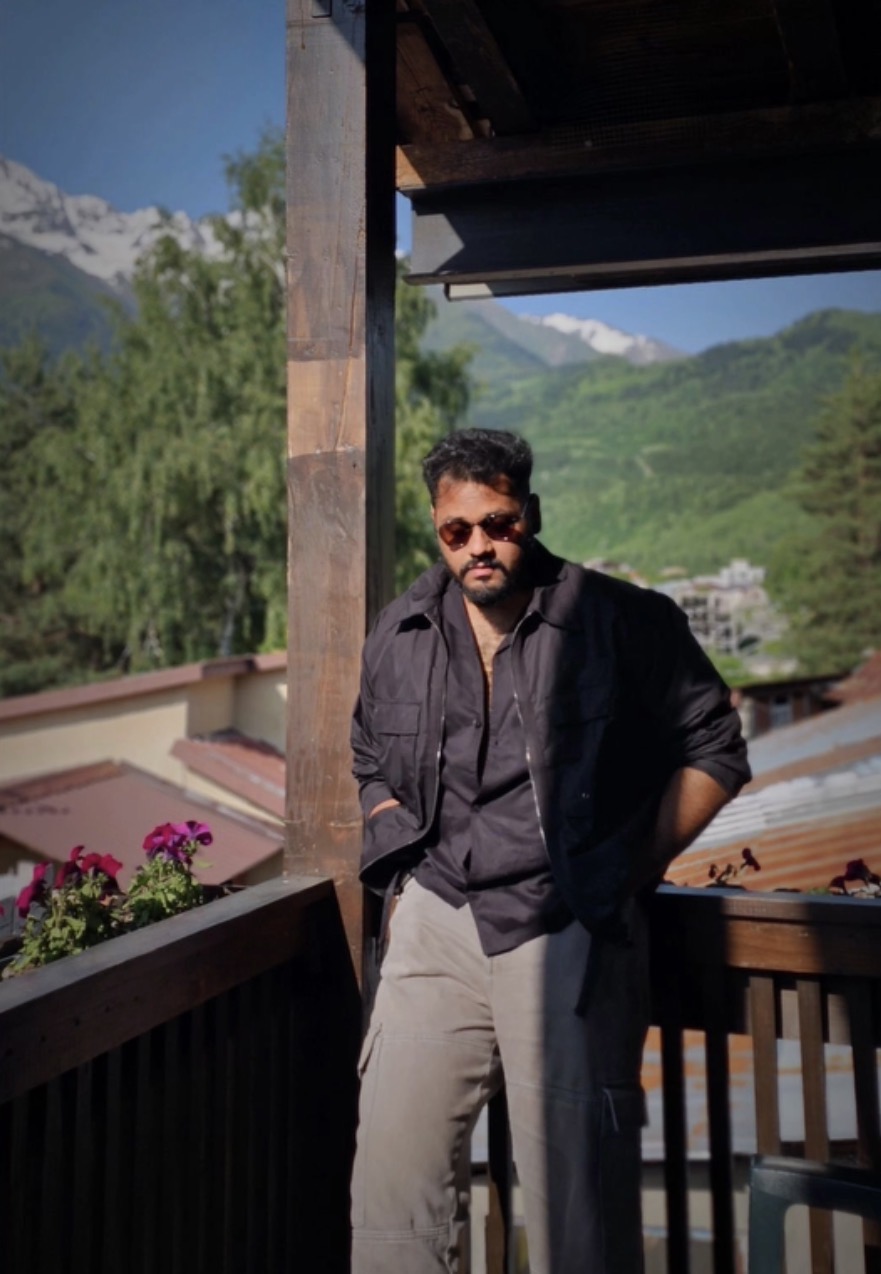 Aman standing on a wooden balcony with green mountains behind him
