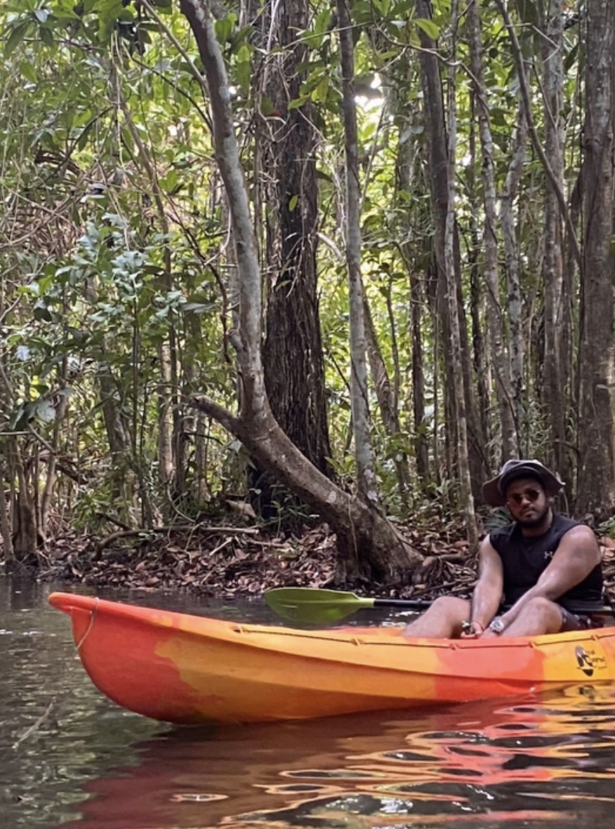 Aman sitting in an orange kayak surrounded by forest